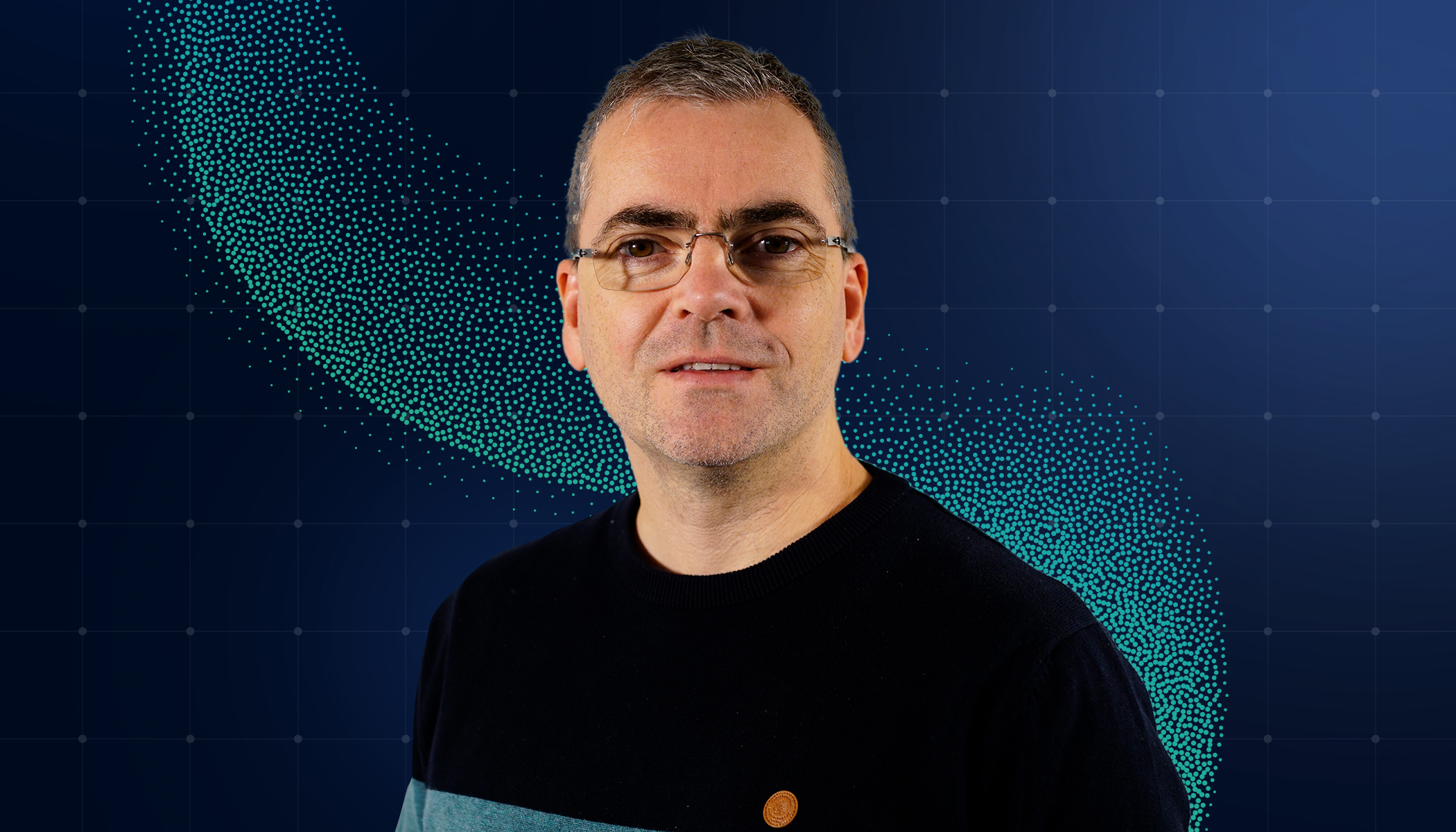 Krystian smiling and wearing glasses and a black t-shirt in front of a blue and turquoise background