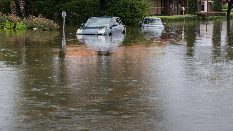 A residential street with cars half submerged in murky flood water