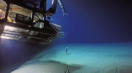 A deep sea diving vessel shining a light on a bank of underwater sand with a dark blue abyss in the background