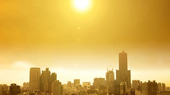 A downtown city area with the sun high in a hazy yellow sky