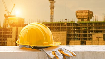 A yellow safety helmet and working gloves placed on building ledge with a large building mid-construction in the background