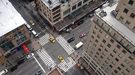 An aerial view of an intersection in a downtown area, with vehicles in the street and pedestrians on the sidewalks