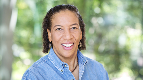 Dawn Wright con una camisa de botones de chambray y sonriendo delante de un fondo con follaje en enfoque suave