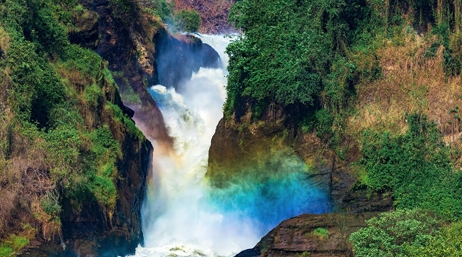 A waterfall surrounded by green, mossy rocks with a rainbow visible in the foreground