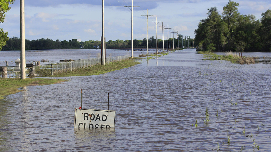 Suburban street deeply flooded with murky blue water with a mostly submerged road closure sign in the foreground
