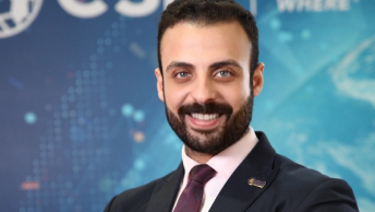 Mohamed El-Sakeet smiling and wearing business attire in front of a blue background