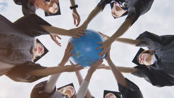 A view from the ground up of people standing in a circle holding one globe in the middle