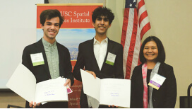 Three students in business clothes holding GIS awards in front of an American flag