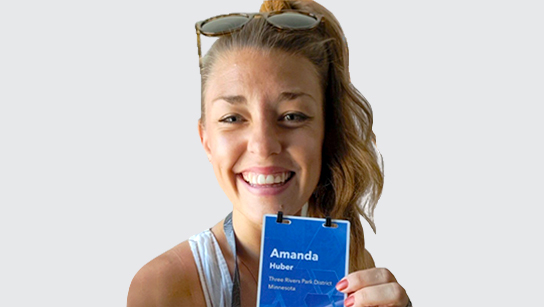 Portrait of Amanda Huber smiling in a white sleeveless top and holding up a conference lanyard with a neutral background