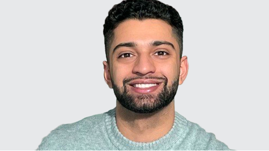 Portrait of Haseeb Malik smiling in a light blue sweater with a pale gray background