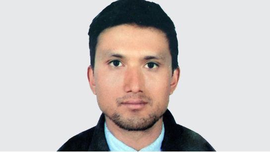Portrait of Pawan Thapa in a pale blue collared shirt and black jacket with a pale gray background