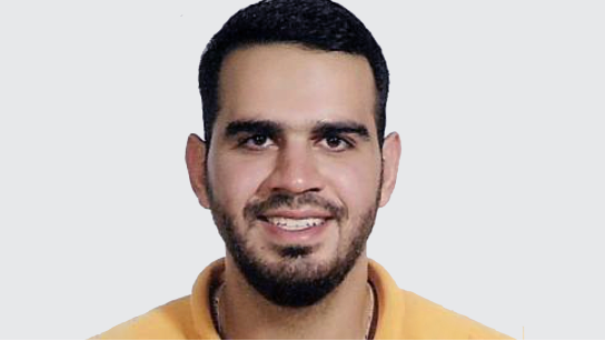 Portrait of Shareef Tarhini smiling in a yellow shirt with a pale gray background