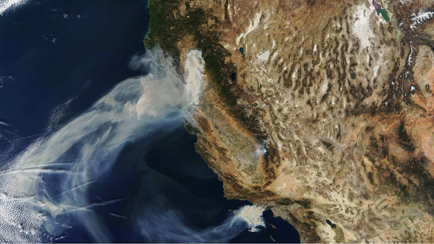 A satellite view of California wildfires emitting large smoke plumes over the Pacific Ocean