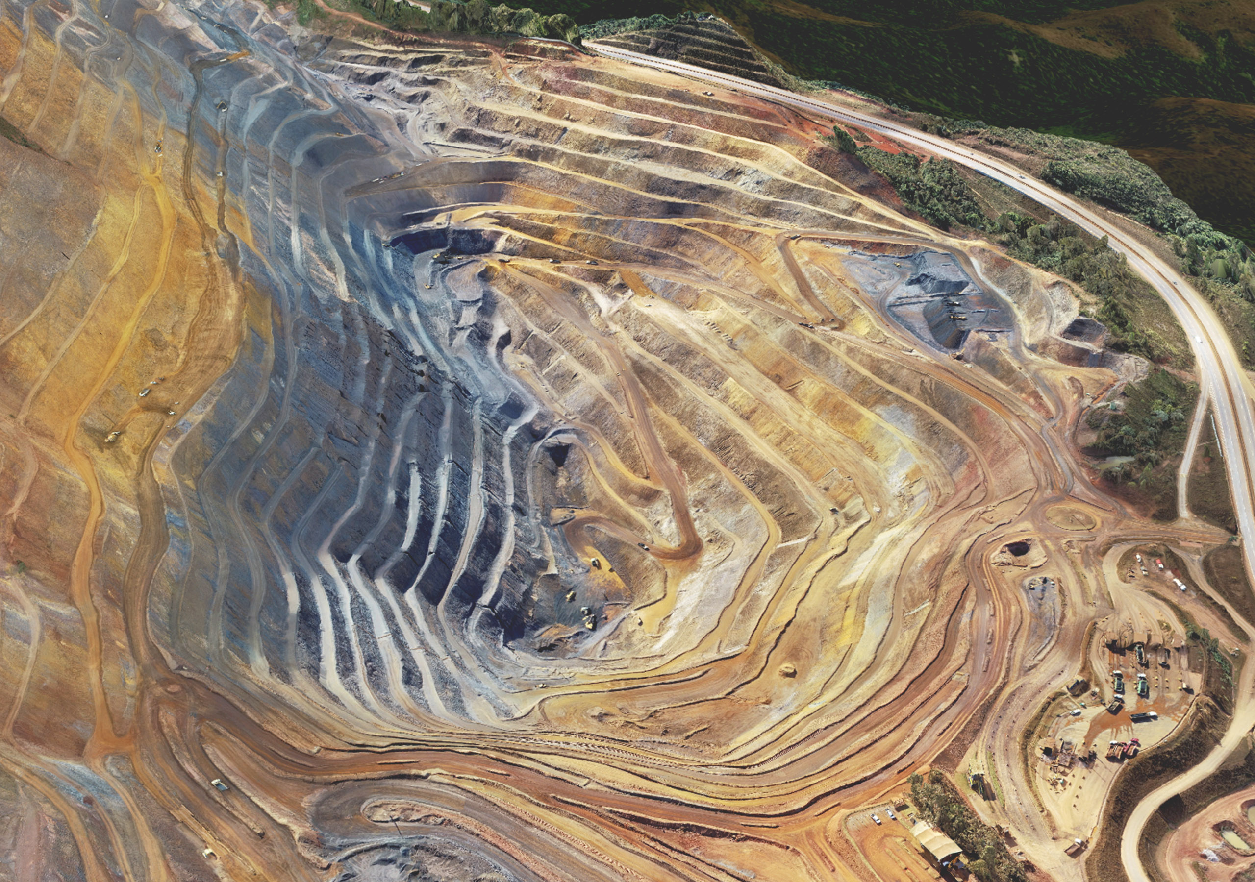 A drone image of a large mining site with terraced paths leading down the side of a mountain into an open pit