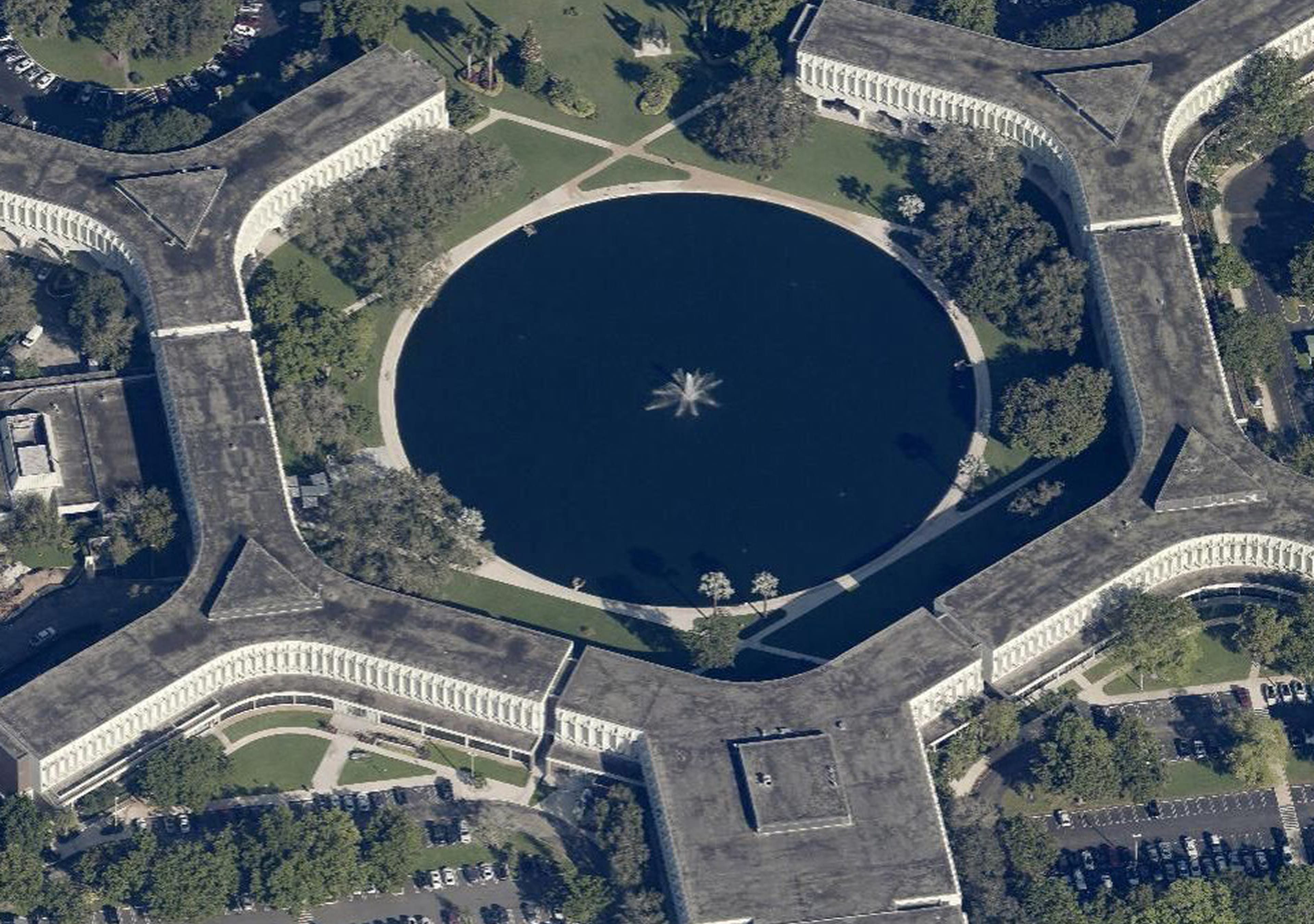 An aerial top-down view of a star-shaped building complex encircling a circular pond with a central fountain