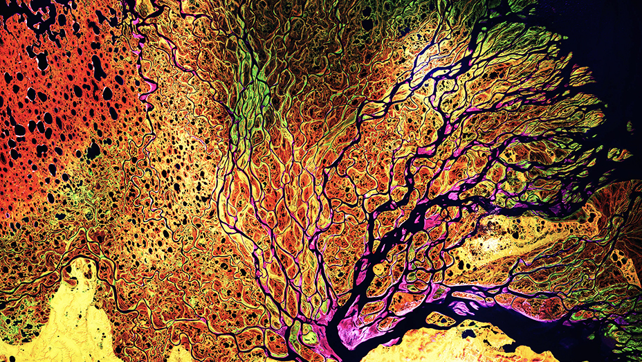 Remote sensing satellite imagery shows a river system surrounded by a landscape colored red, brown, green, yellow, and pink