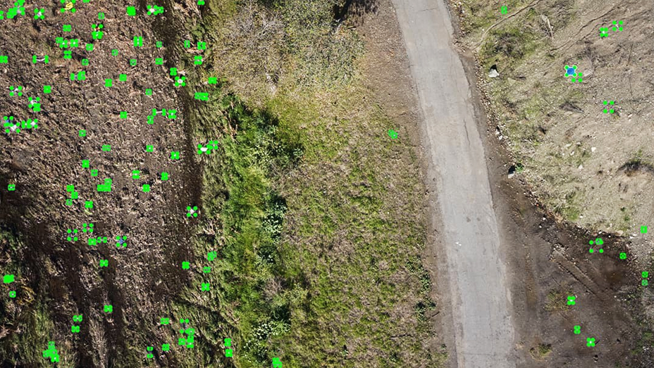 Drone imagery shows the landscape next to a narrow road, with green dots where a machine learning model has identified trash