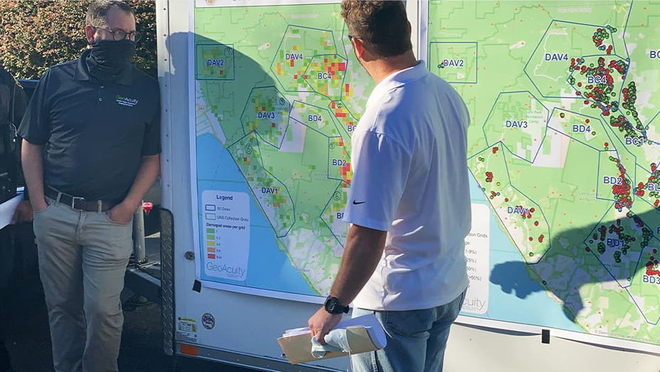 Two men look at a large printed map showing wildfire hotspots as red polygons