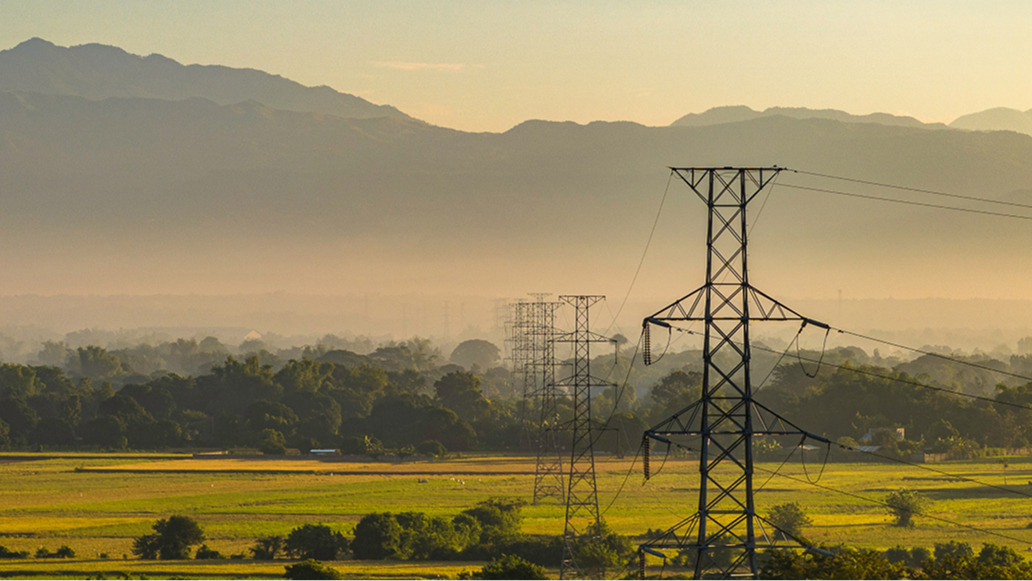 A line of utility towers with a mountain range in the distance on a hazy day