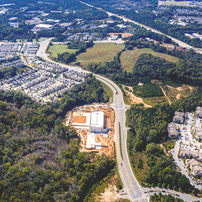 An aerial image of a four-lane road winding through a suburban area with residential neighborhoods and forested land.