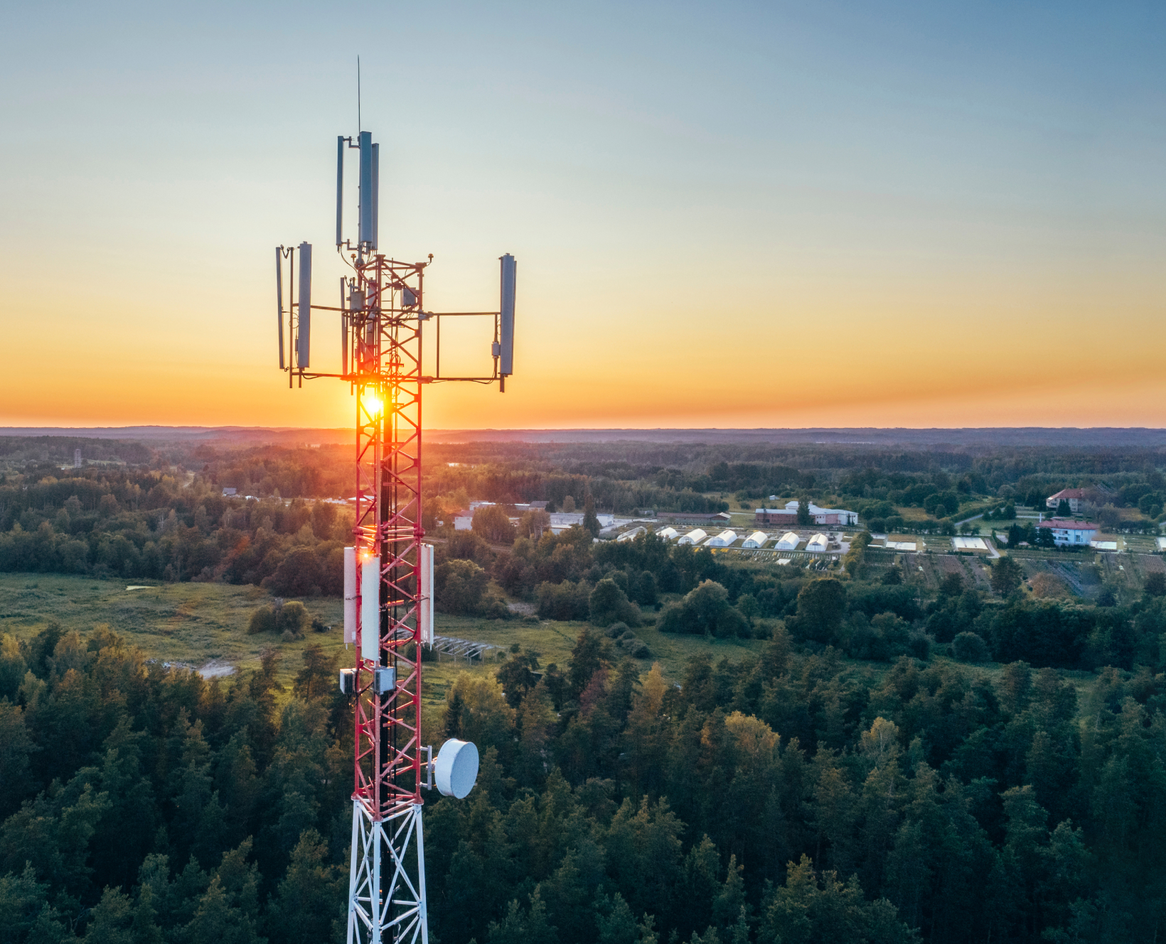 An image of a tall red and white cell tower and green trees in the background