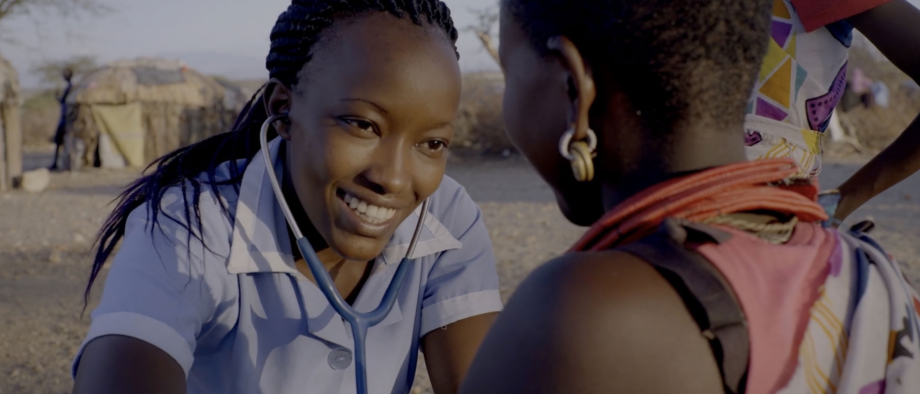 An image of a smiling nurse listening to the heart of a patient with a stethoscope in a rural setting