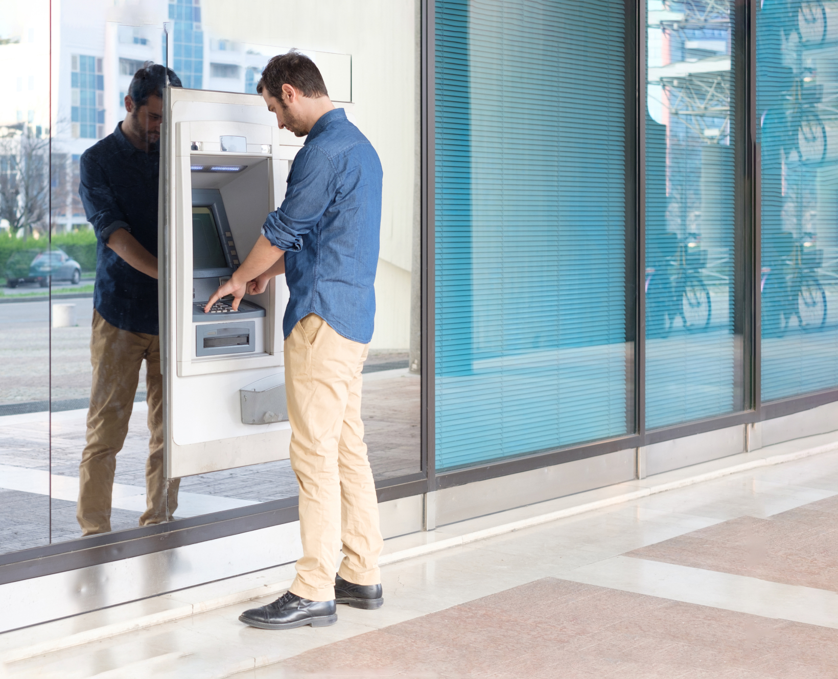 An image of a man dressed in a blue shirt and khakis at an ATM machine