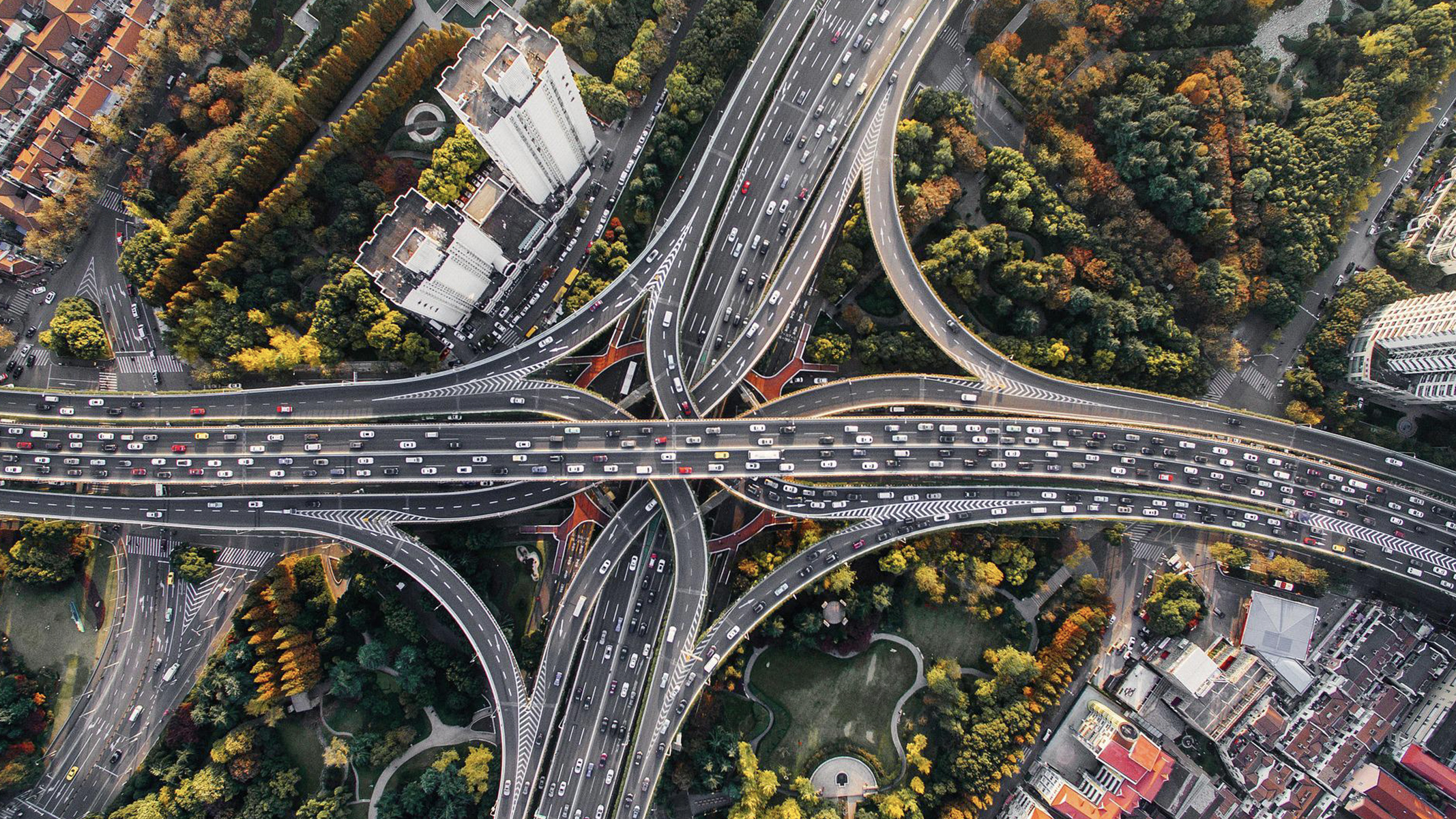 Aerial view of a busy multi-freeway intersection with underpasses and overpasses, surrounded by trees and buildings