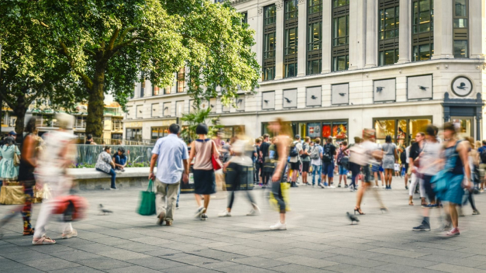 Centro commerciale soleggiato all'aperto con molte persone in abbigliamento casual che camminano in ogni direzione