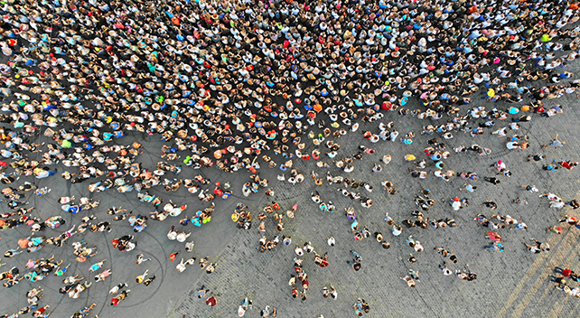 Foto aerea di una folla colorata di persone strettamente raggruppate su una strada di cemento e ciottoli