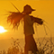 A person in a wide brim hat carrying a bundle of harvested wheat through a field backlit by a bright sun in a yellow sky