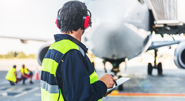 Aircraft inspector wearing aviation headphones and holding a tablet inspecting an airplane