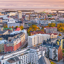Aerial view of a city during autumn, featuring colorful residential buildings, a large park with vibrant yellow and orange foliage, and high-rise buildings, industrial zones, and a harbor with docked ships 