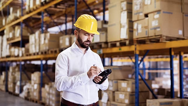Man wearing a yellow hard hat in a warehouse using a tablet 