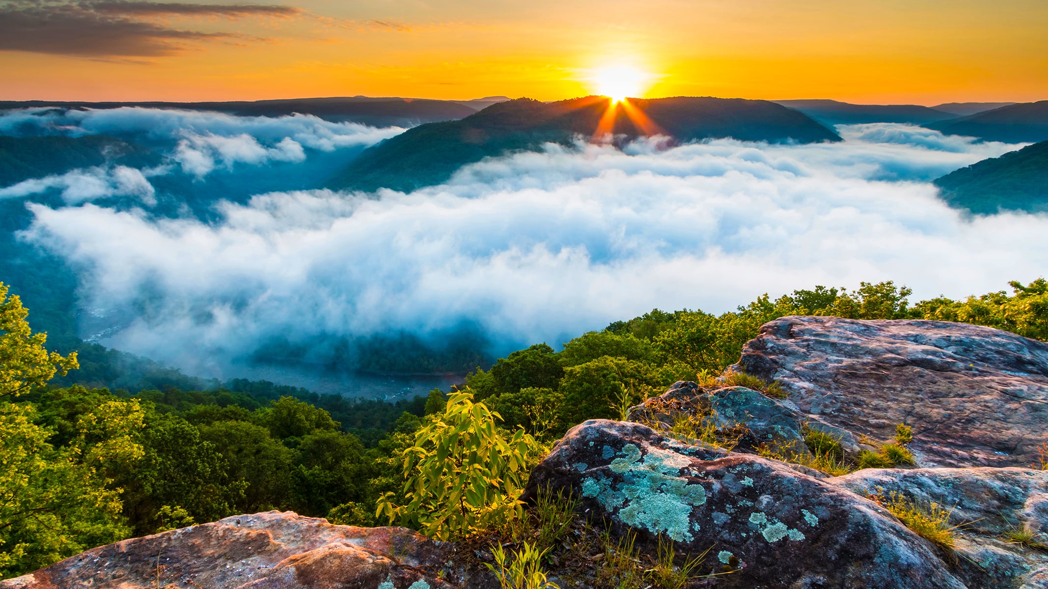 A sunrise view overlooking fog‑filled valleys and rocky cliffs, with warm light illuminating the landscape