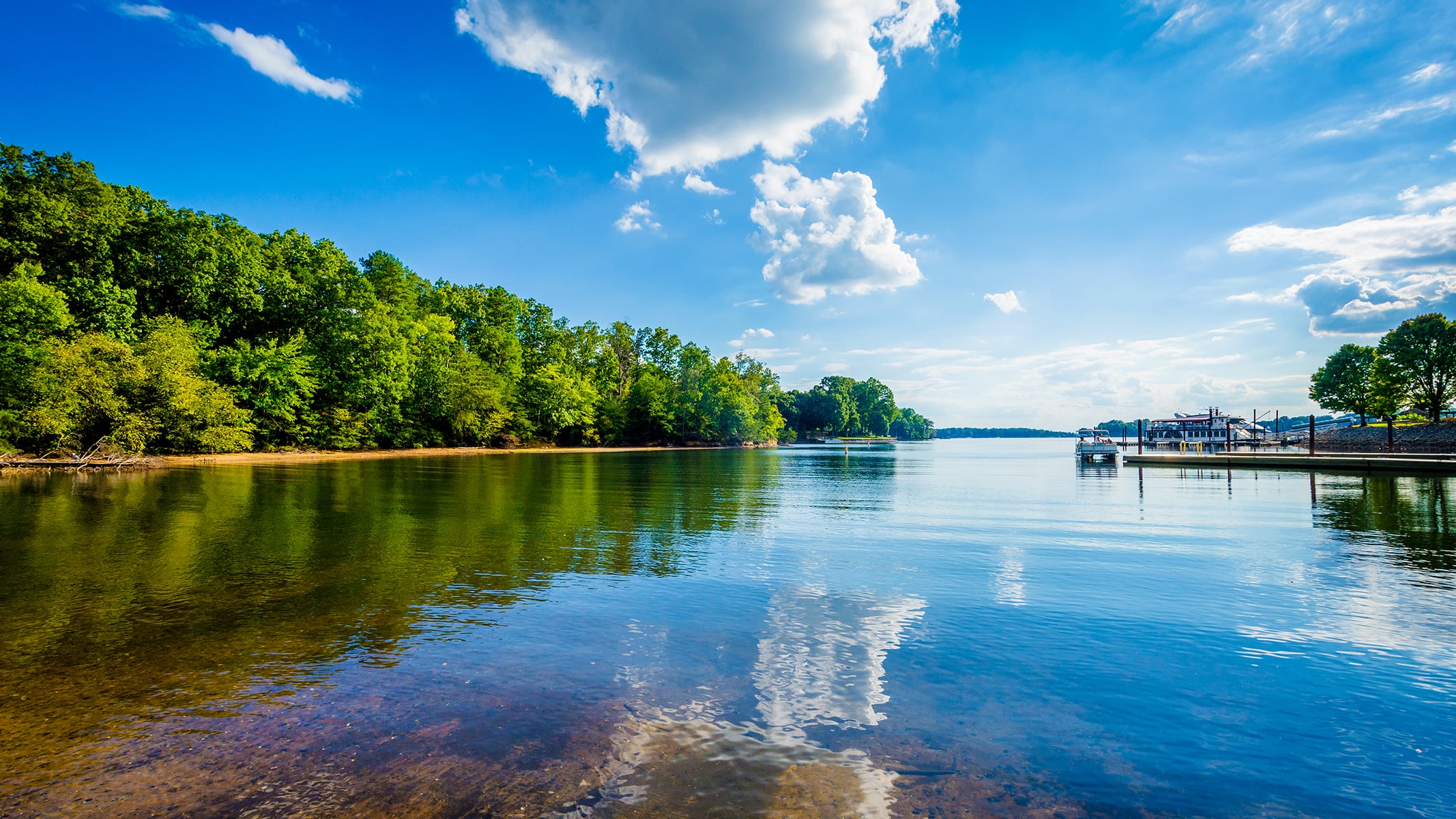 A wide valley with agricultural fields, a river, and tall mountains rising in the background under a partly cloudy sky