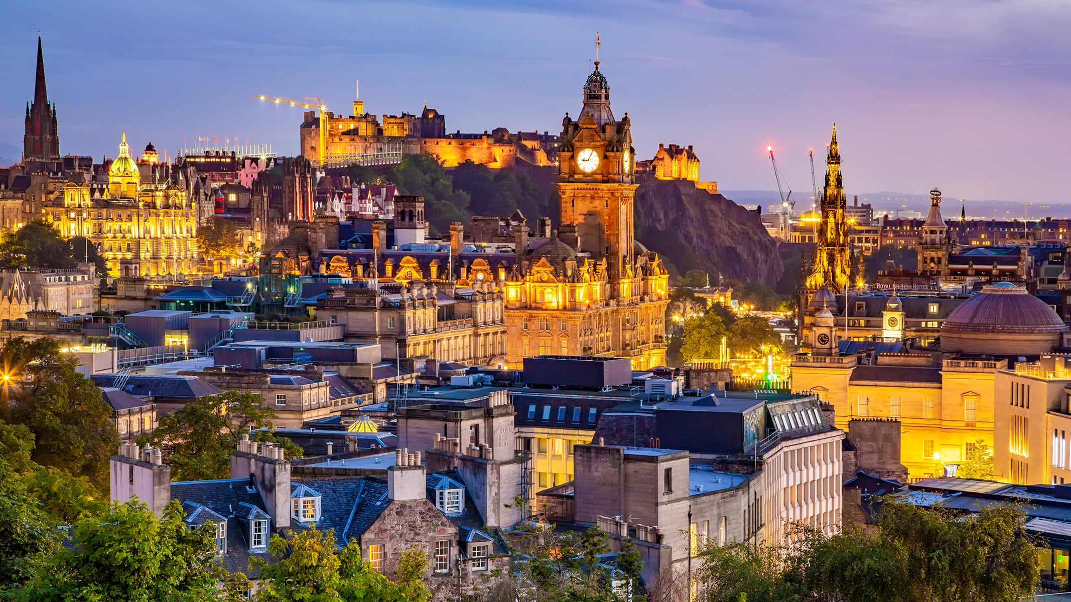 An evening cityscape with historic buildings and warm lights glowing across a dense urban skyline