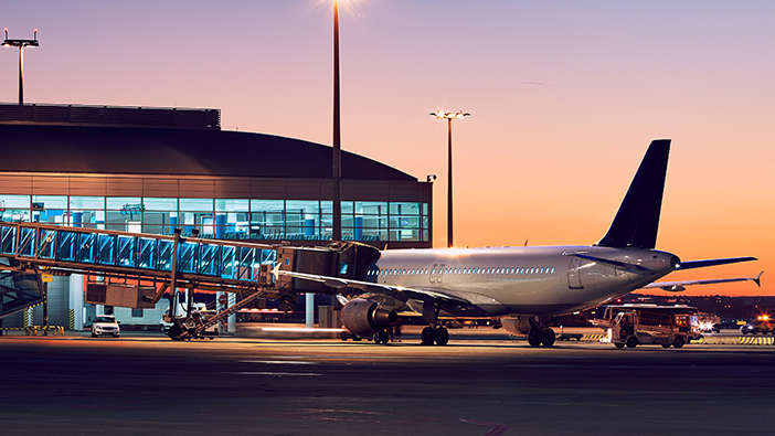 Flughafen mit großer Glasfront und einem Flugzeug auf der Landebahn in der Abenddämmerung