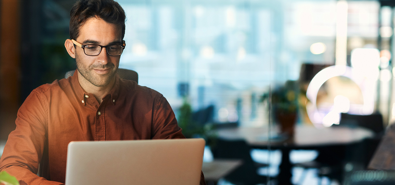 Eine lächelnde Person, die vor einem Laptop sitzt und arbeitet