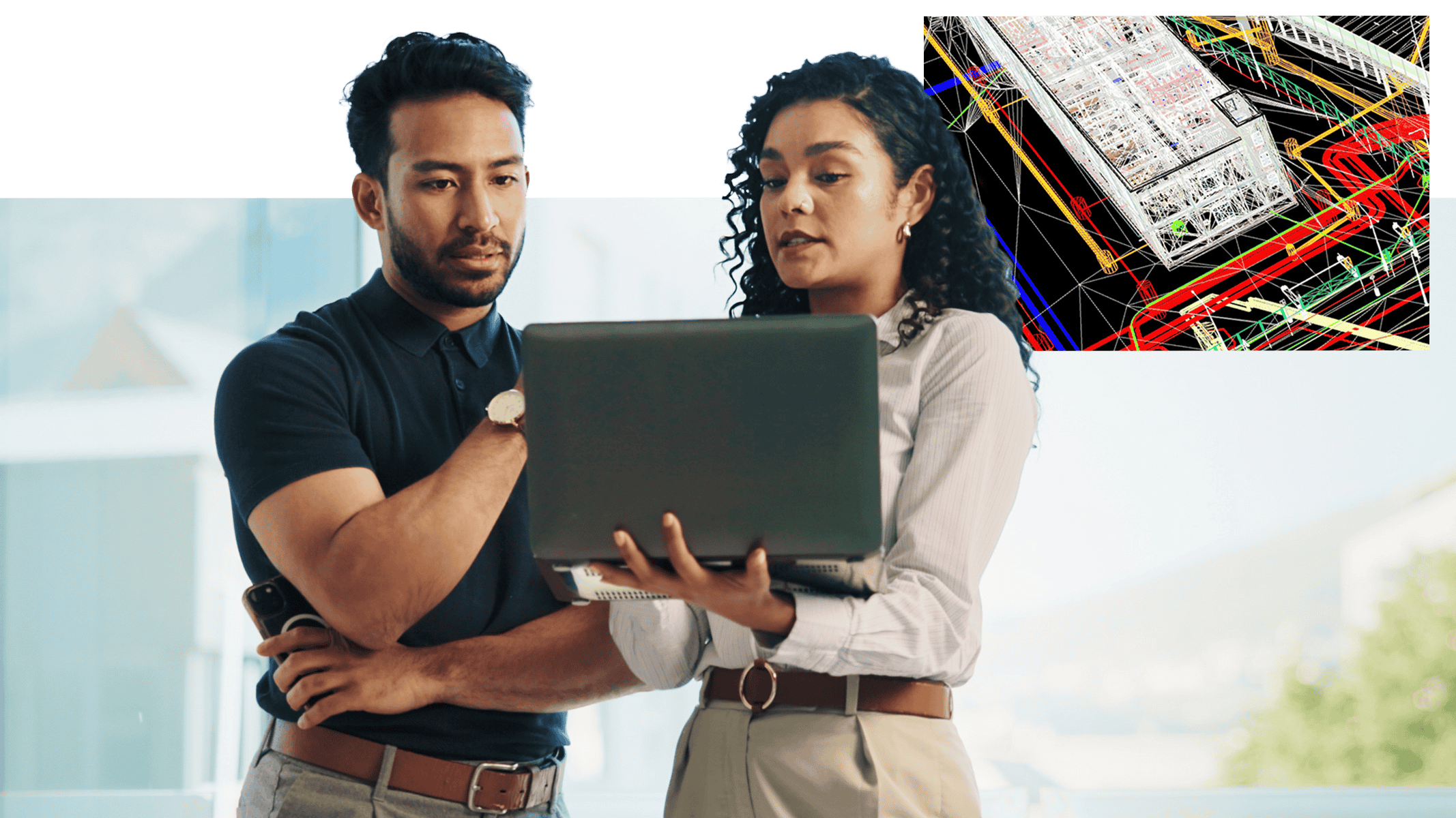 Two professionals standing together and reviewing information on a laptop, with a colorful technical diagram displayed in the upper corner