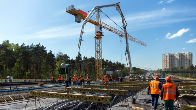 A tree-lined highway construction site with a yellow crane and many people working in orange vests