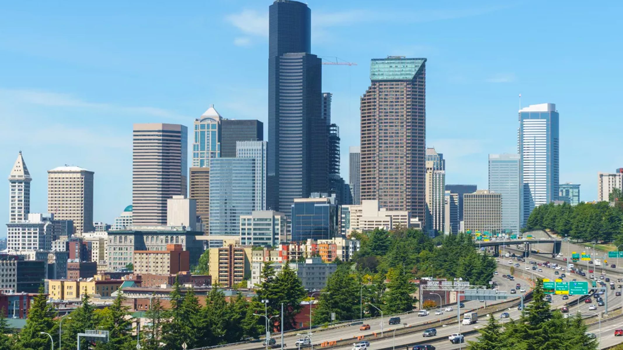 Seattle skyline on a sunny day with a busy highway in the foreground.