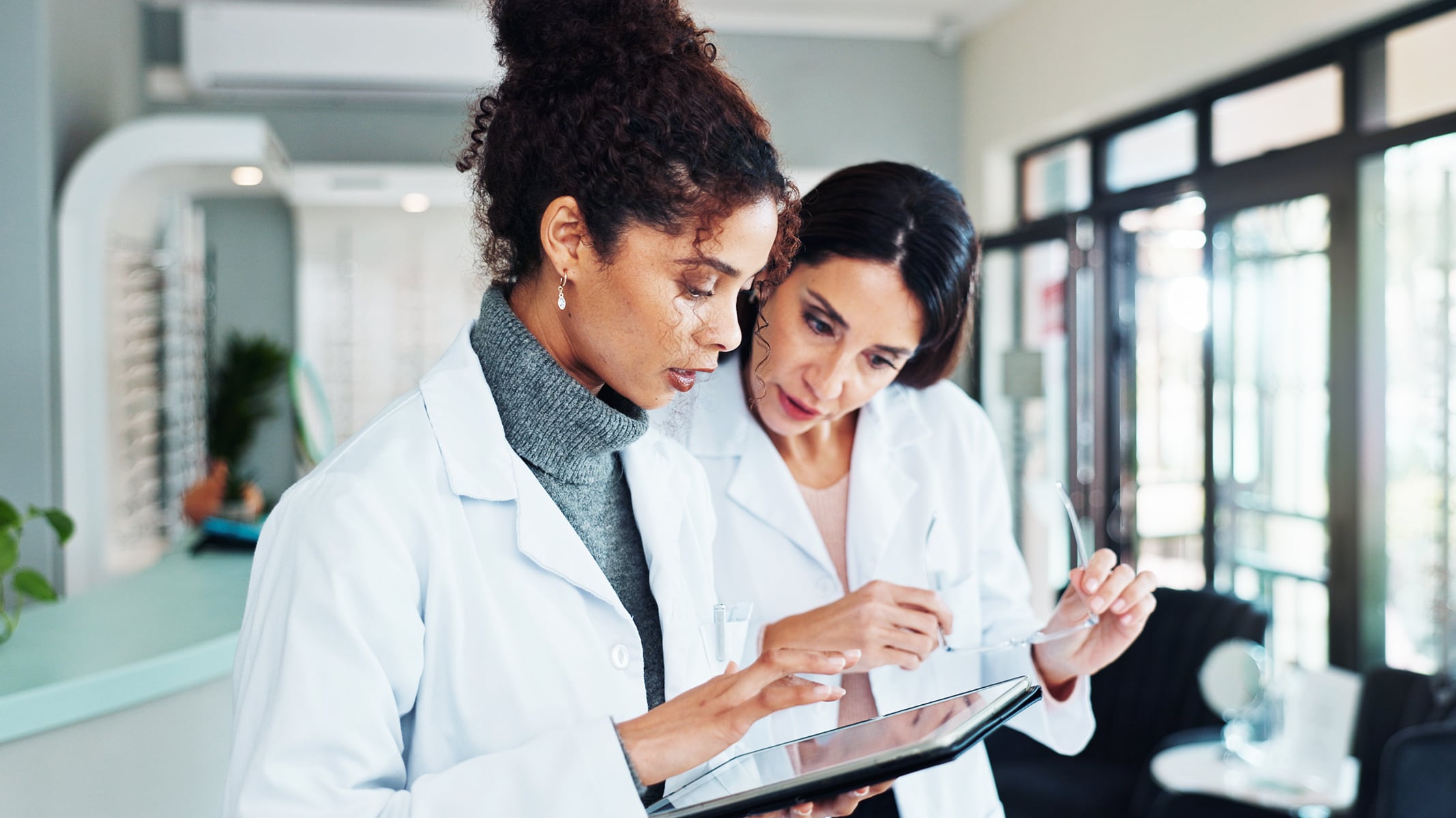 Two healthcare professionals in white lab coats looking at a tablet in a healthcare facility