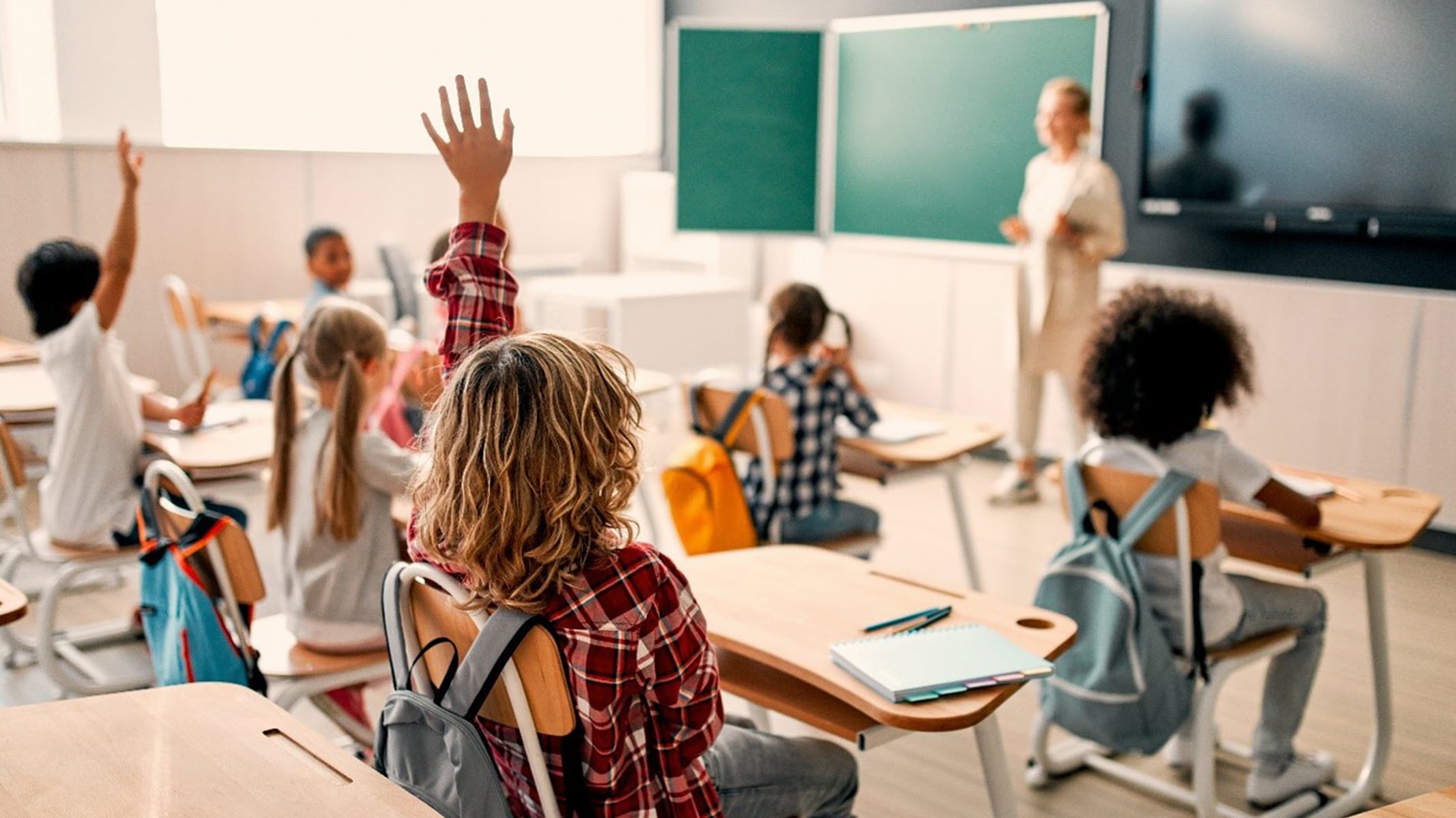 Children seated in a classroom with one raising their hand