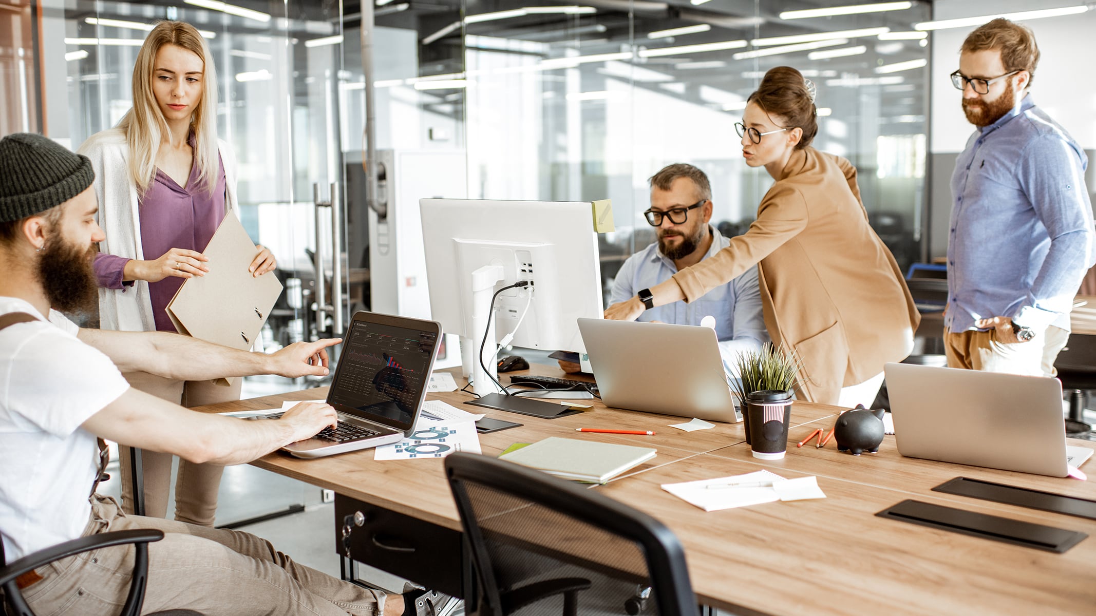 Five people in an office workspace interacting and working on computers