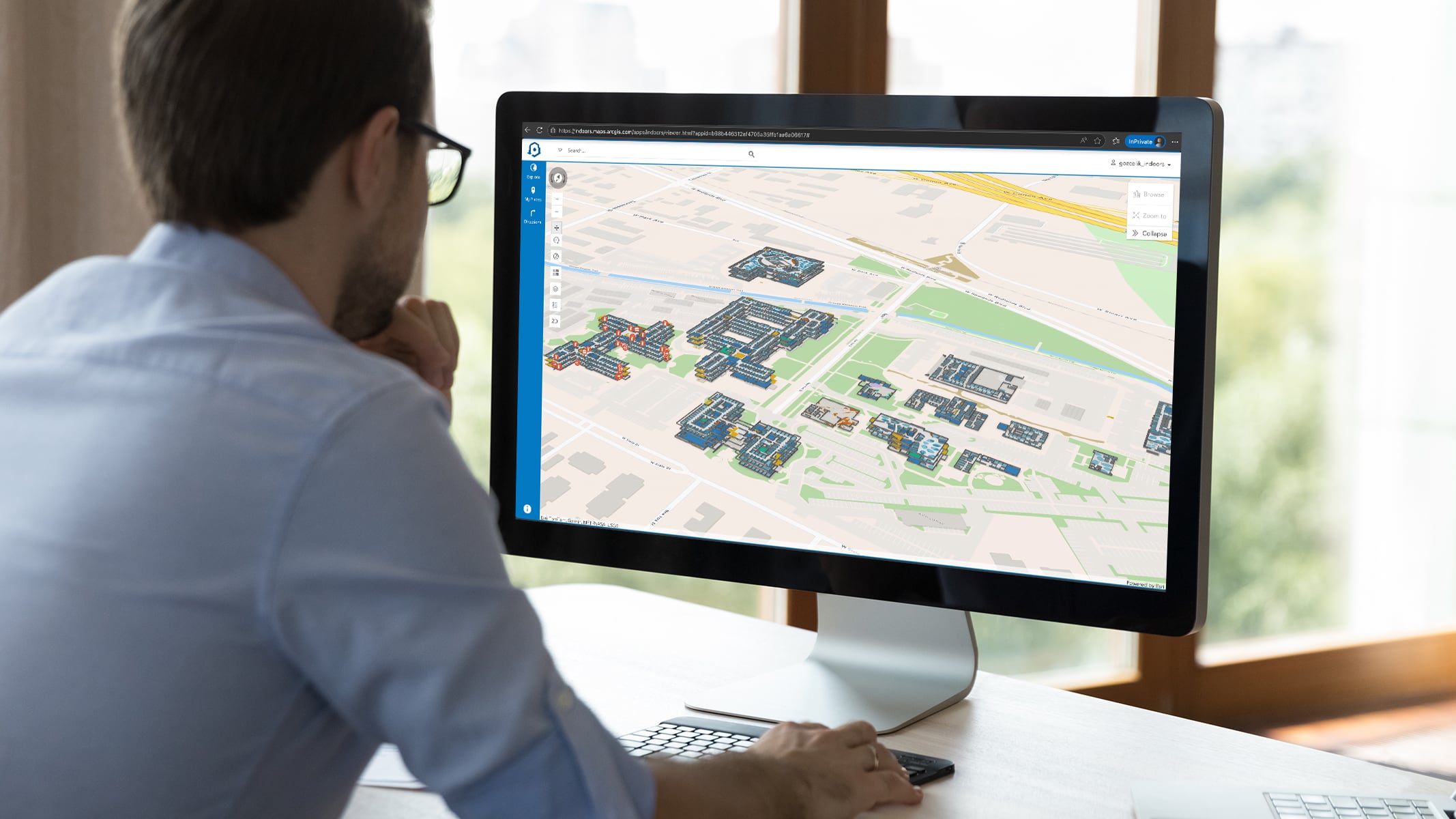 Person seated at a desk looks at a 3D indoor map of a building complex on a computer monitor