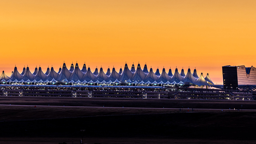 Denver Airport seen from a distance with numerous tentlike shapes silhouetted against a vivid orange sunset