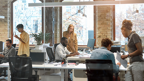 Gruppe von Personen in einem Büro, die an verschiedenen Schreibtischen arbeiten und Dokumente lesen