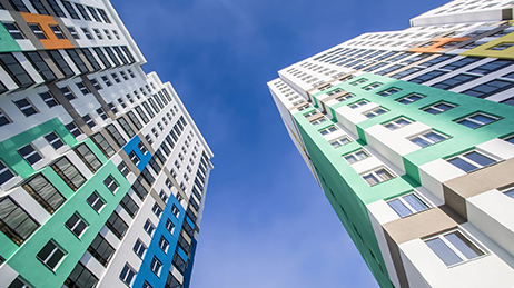 Two multicolored high-rise apartment buildings in green, blue, and white against a blue sky with clouds
