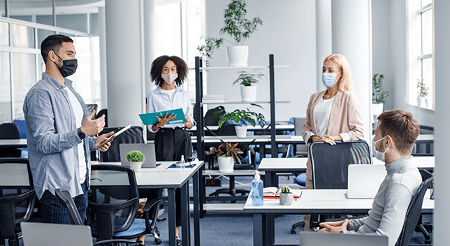 Four socially distanced workers in an office wearing protective face masks, having a conversation